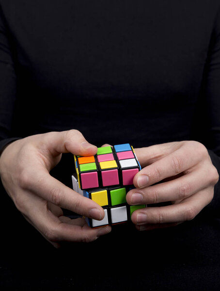 a man dressed in black holding a multicolored cube