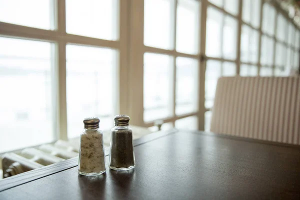 Zout en peper in glazen potten op een tafel in de buurt van de grote ramen — Stockfoto