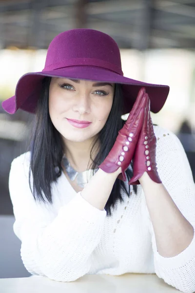 Mysterious young woman in a burgundy hat and gloves sits at a ta — Stock Photo, Image