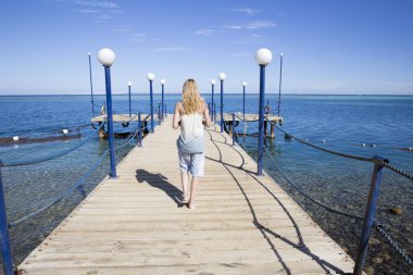 Ahşap iskele w üzerinde yürüyen uzun saçlı güzel genç sarışın