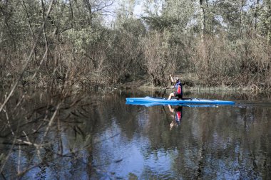 Yasak boyunca sakin bir nehirüzerinde mavi bir kano üzerinde kürek genç bir adam