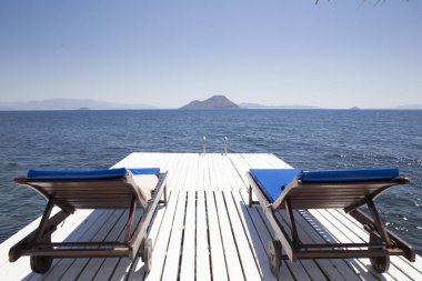 Deniz agains tarafından beyaz bir rıhtımda iki beyaz ahşap plaj sandalye