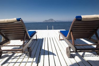 İki denizin kenarında beyaz bir ahşap iskele üzerinde ahşap sandalye beyaz 