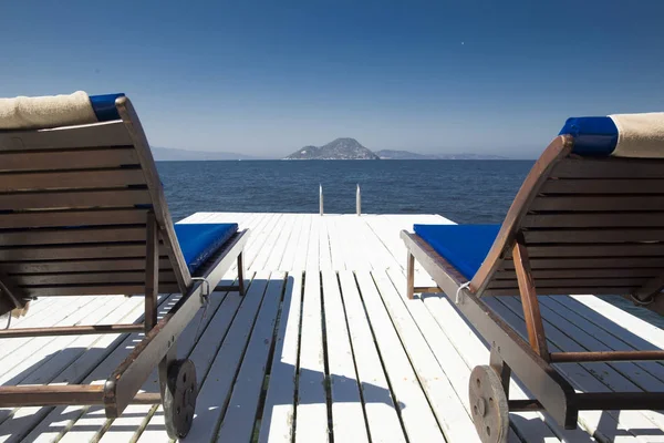 İki beyaz ahşap plaj kanepe bir tahta iskele üzerinde mavi denize yakın: