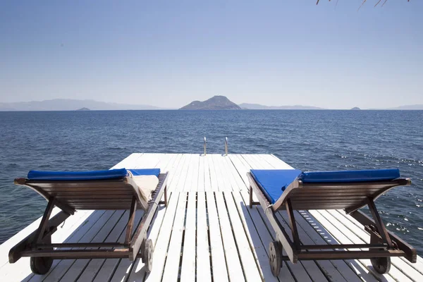 Deniz agains tarafından beyaz bir rıhtımda iki beyaz ahşap plaj sandalye