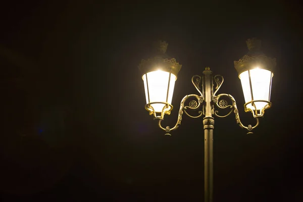 Uma lâmpada de rua forjada acesa com duas lâmpadas e um brilho de luz aceso — Fotografia de Stock