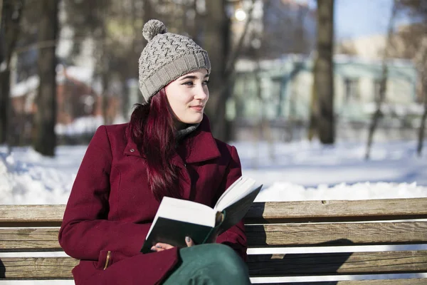 Young girl in a hat and a burgundy jacket, sitting with a book o — Stock Photo, Image