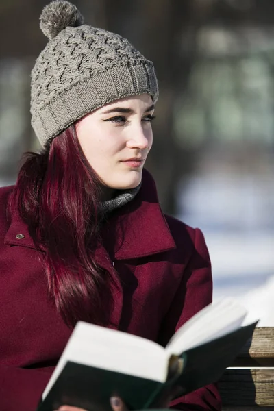 A young girl in a hat and a burgundy jacket sits lost in though — Stock Photo, Image