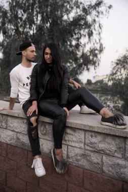 aşık çift: siyah giysili bir beton parapet mesafe yüksek binaların bir arka plan üzerinde bir parkta oturan bir şık genç sarılma gülümseyen güzel bir genç kız