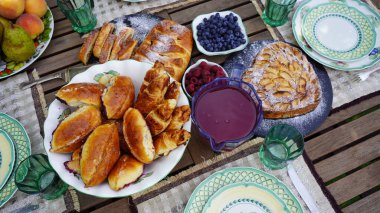 Meyve reçeli dolu taze hamur işleriyle servis edilen ahşap masa ve bulanık bir bahçe arka planında meyve ve böğürtlen.
