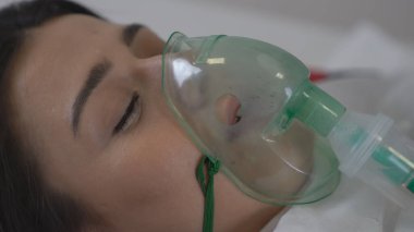 Bir kadın hasta koronavirüs enfeksiyonu geçirdiği için solunum ve oksijen alır. Bir doktor arka planda pozitif test tüpü gösteriyor..