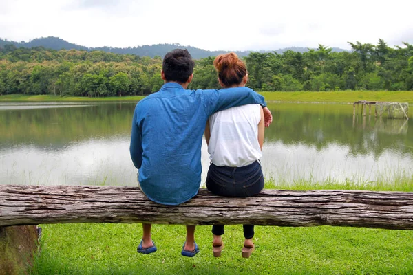 恋爱中的年轻夫妇一起坐在湖边的木柴上 带着山林的景色 与丈夫和妻子共度美好快乐的时光 — 图库照片