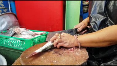Aşçı, ahşap tahtada taze balık kesiyor ve mutfak odasında satılık yemek pişiriyor. Balık filetosu ve bir hayvanı öldürmek.