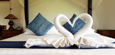 Beautiful white towel folded in two swan shape or heart with blue pillow and wall background on bedroom in hotel - Beautiful design and Idea for decoration room and dweller concept   clipart