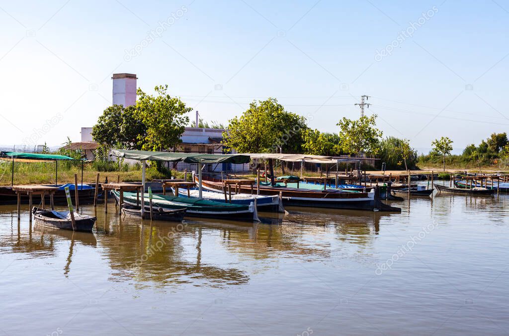 Wooden boats moored at the harbor pier for walks on Lake Albufera with rice paddies in the background and blue sky.