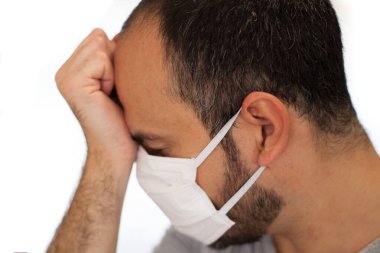 Coronavirus hastası bir adam maske takar ve ateş, yorgunluk ve baş ağrısı gibi semptomlardan dolayı alnına dokunur..