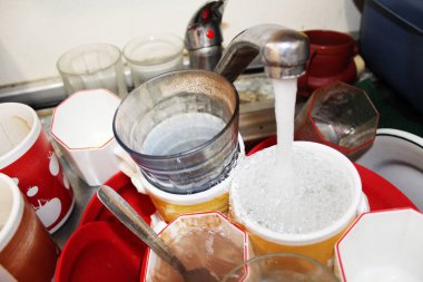 Kirli bulaşıklar ve bardaklar lavaboda temizlenmeden ve açık musluk suyu harcamadan birikmiş.