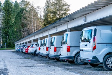 Beyaz renkli araba ve minibüslerin olduğu park yerindeki fotoğrafı kapat. Güneş ve yağmurdan korunan çatılar, kar. Farklı hava koşulları için güvenli İskandinav taşımacılık işi