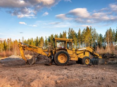 Orman kazıları için garajın yanında duran eski sarı kazıcının sol tarafını kapatın ve yeni bina için hazırlık yapın. Kuzey İsveç, Umea. İskandinav inşaat endüstrisi. Güneşli, mavi gökyüzü