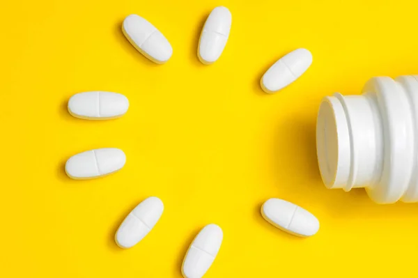 Comprimidos blancos sobre fondo amarillo caen de un frasco blanco . — Foto de Stock
