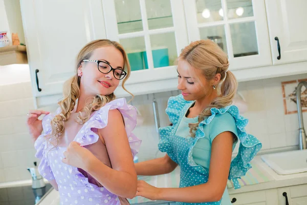 Two friends in the kitchen helping each other to tie the apron