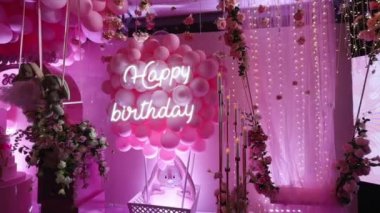 Pembe balonların, yapay mumların ve partideki güllerin arka planında parlayan mutlu doğum günü mesajı.