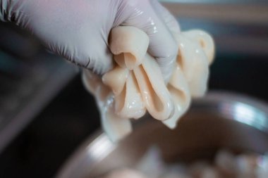 Lavaboda su ve eldivenle mürekkep balığını temizleyen biri. Bu mürekkep balığı yemek pişirmek için kullanılacak. Mürekkep balığı halkaları metal bir kapta olacak..