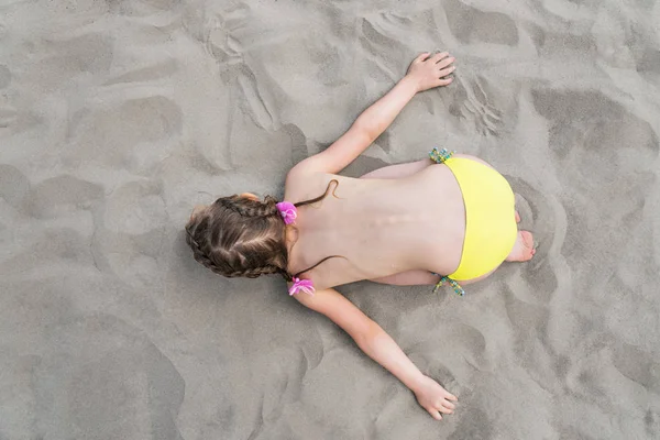 Child represents airplane lying on the sand — Stock Photo, Image