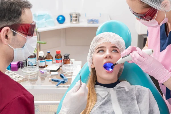 Dental assistant shines with ultraviolet lamp in patient open mouth