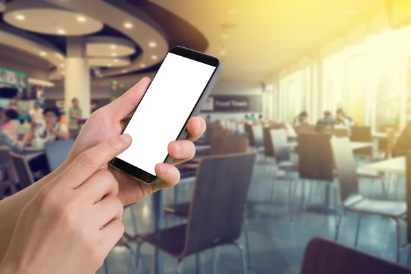 Mano humana y el teléfono inteligente táctil con pantalla en blanco en fondo borroso patio de comida . —  Fotos de Stock