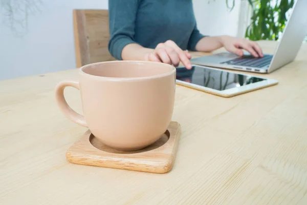 Mesa de oficina con taza de café y la mujer que trabaja usando el ordenador portátil en h — Foto de Stock