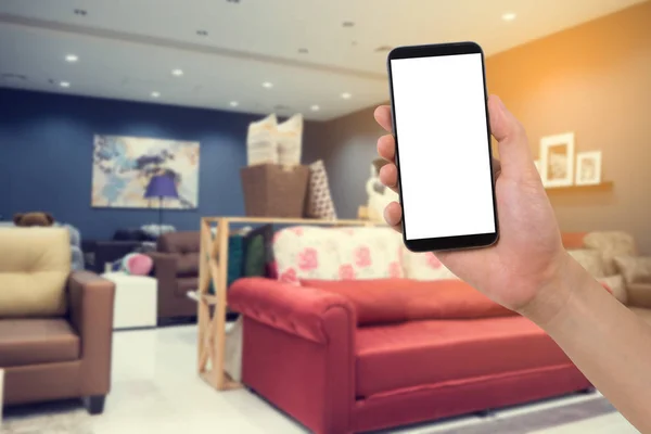 Mão humana segurar smartphone, tablet, telefone celular na loja de móveis Home embaçado, conceito de encomendar decoração home online . — Fotografia de Stock