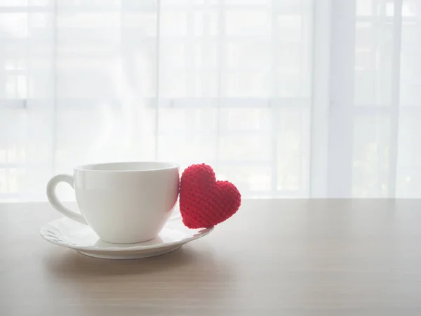 Mesa de oficina de madera con taza de café caliente y símbolo de forma de corazón rojo — Foto de Stock