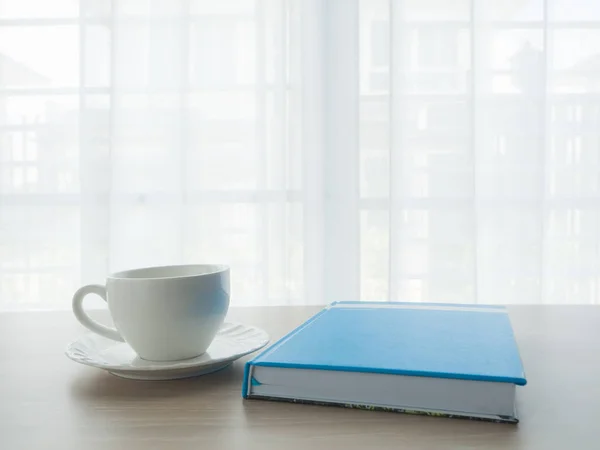 Mesa de oficina de madera con taza de café blanco y papel portátil azul — Foto de Stock
