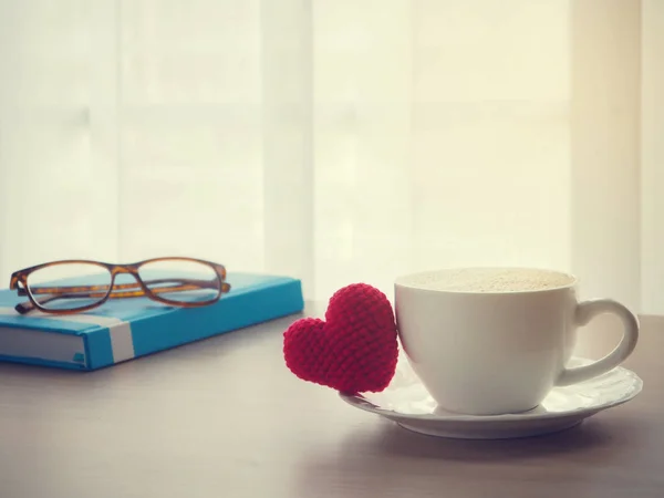 Mesa de oficina de madera con signo de forma de corazón rojo en la taza de café con leche — Foto de Stock