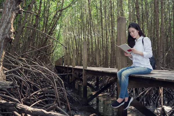 Junge asiatische Frau in blauer Jeans und weißem Hemd liest Buch auf — Stockfoto