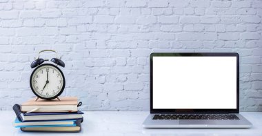 Kitap yığınındaki klasik saat ve boş ekran dizüstü bilgisayar, onunla defter.