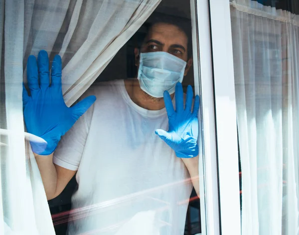 COVID-19 Pandemic Coronavirus Doctor with mask in hospital or home isolation auto quarantine for virus SARS-CoV-2. Man voluntary isolation with surgical mask looking outside. Disease 2019.