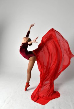 Kırmızı elbiseli bir jimnastikçi beyaz arka planda kırmızı bir pareo ile dans ediyor.