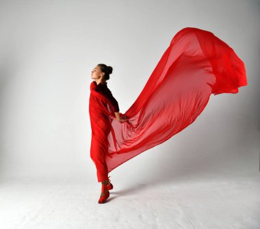 Kırmızı elbiseli bir jimnastikçi beyaz arka planda kırmızı bir pareo ile dans ediyor.