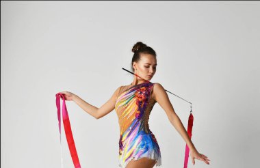 Beyaz arka planda kırmızı kurdeleyle dans eden parlak takım elbiseli bir jimnastikçi.