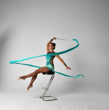 Mavi takım elbiseli, mavi kurdeleli bir jimnastikçi sandalyede oturuyor.