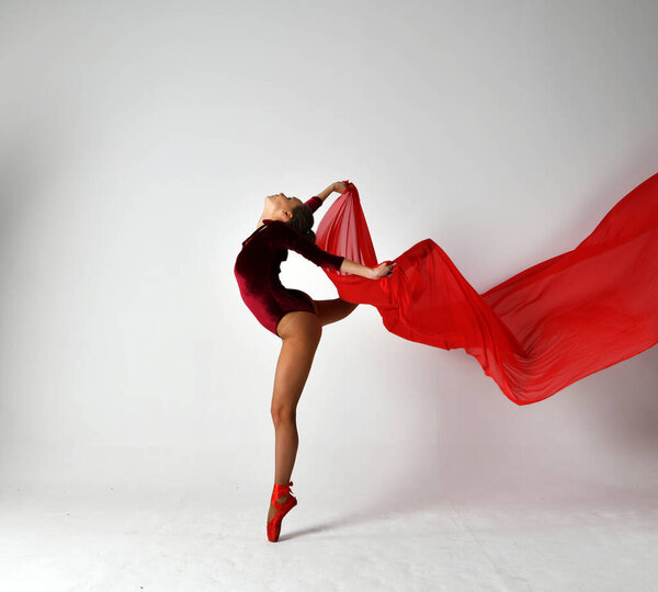 Gymnast in a red suit dancing with a red pareo on a white background