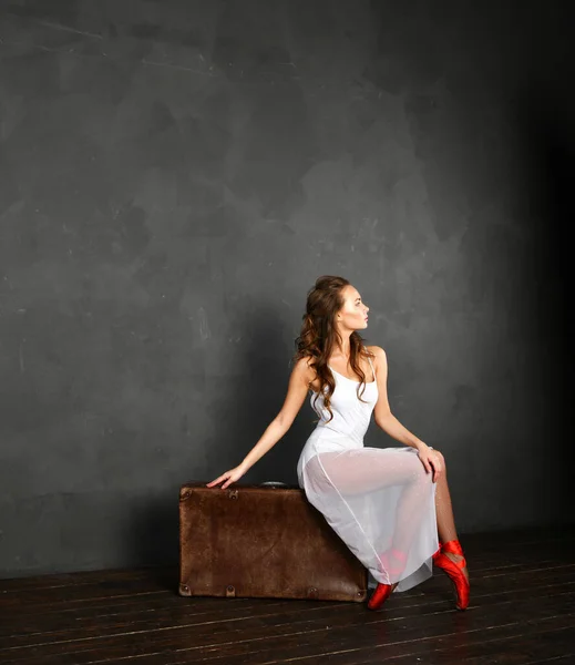 Balerina Fehér Ruhában Piros Hegyes Egy Bőröndön Szürke Háttér — Stock Fotó