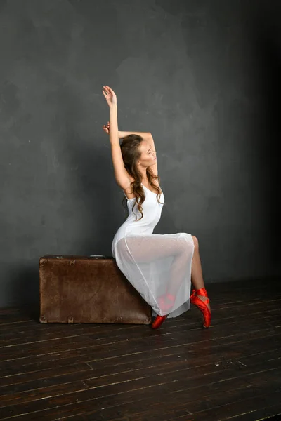 Bailarina Vestido Branco Pointes Vermelho Senta Uma Mala Fundo Cinza — Fotografia de Stock