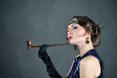Siyah eldivenleri ve piposu olan mavi bir gece elbisesi içinde güzel bir kadın.