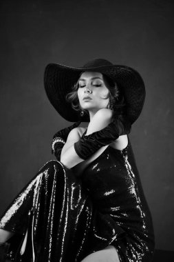 Mavi gece elbisesi içinde siyah eldivenli güzel bir kadın masada oturuyor.