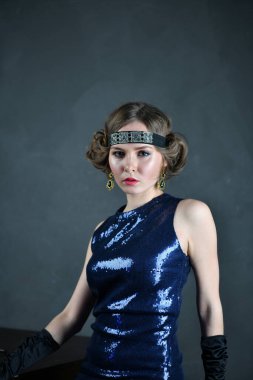 Mavi gece elbisesi içinde siyah eldivenli güzel bir kadın masada oturuyor.