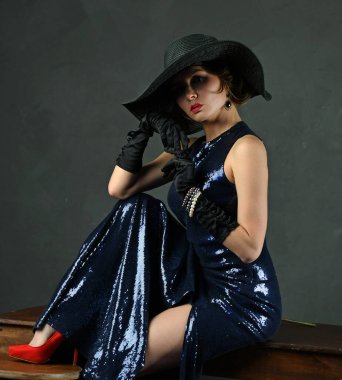 Siyah eldivenli, siyah şapkalı ve silahlı, mavi gece elbisesi giyen güzel bir kadın.