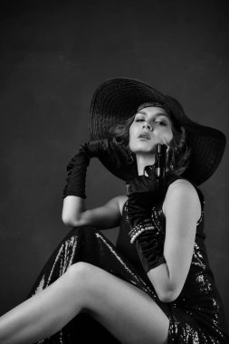 Siyah eldivenli, siyah şapkalı ve silahlı, mavi gece elbisesi giyen güzel bir kadın.